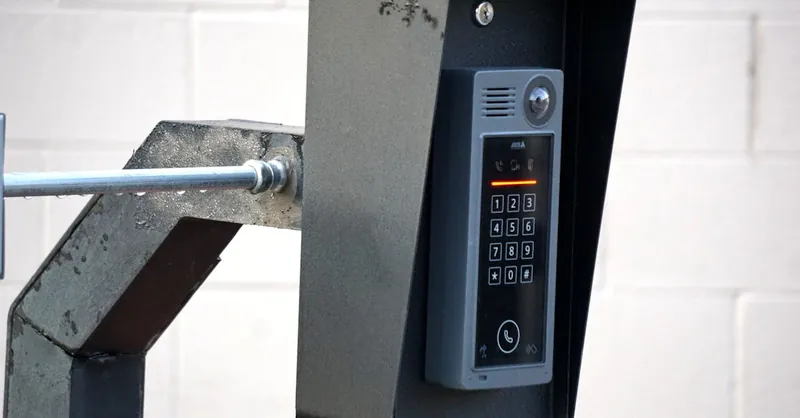 Close-up of a modern security intercom and keypad mounted on a wall outdoors with visible wiring.