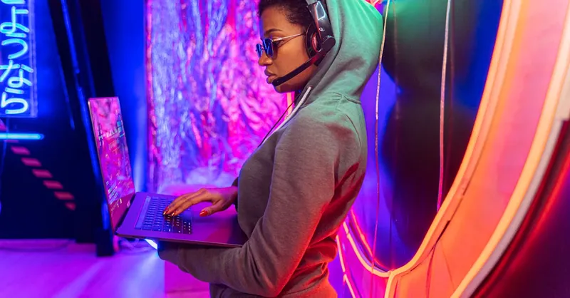 A tech-savvy individual using a laptop in a neon-lit room, symbolizing cybersecurity.