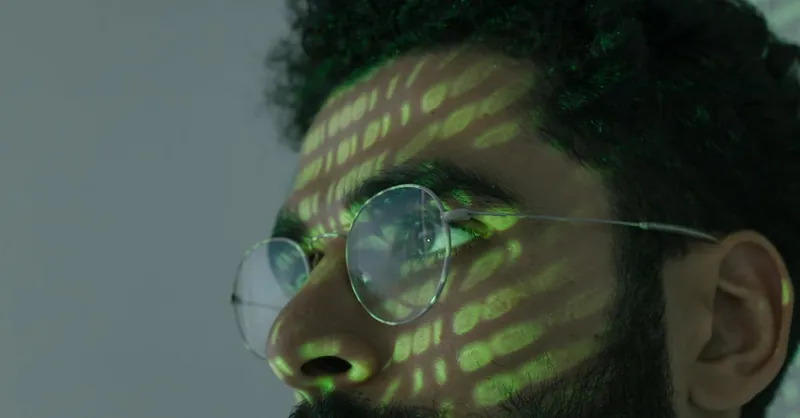 A man wearing glasses with binary code projected across his face, symbolizing cybersecurity.