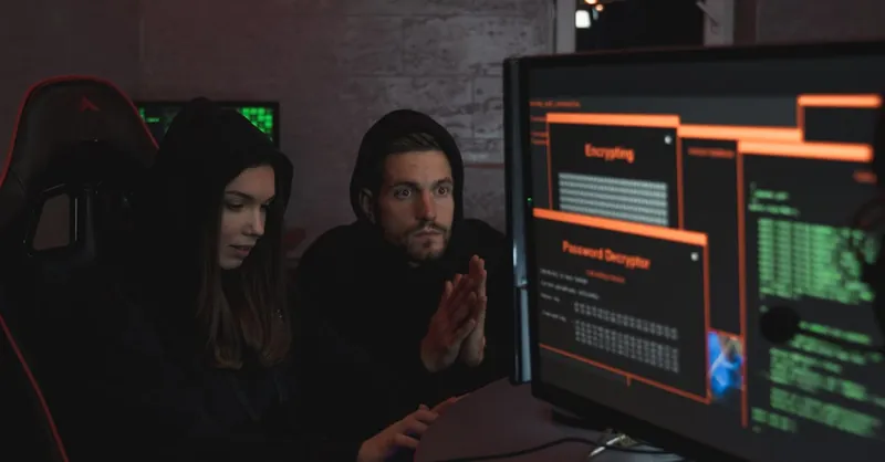 Cybersecurity experts in hoodies analyzing encrypted data on computer screens in an indoor setting.