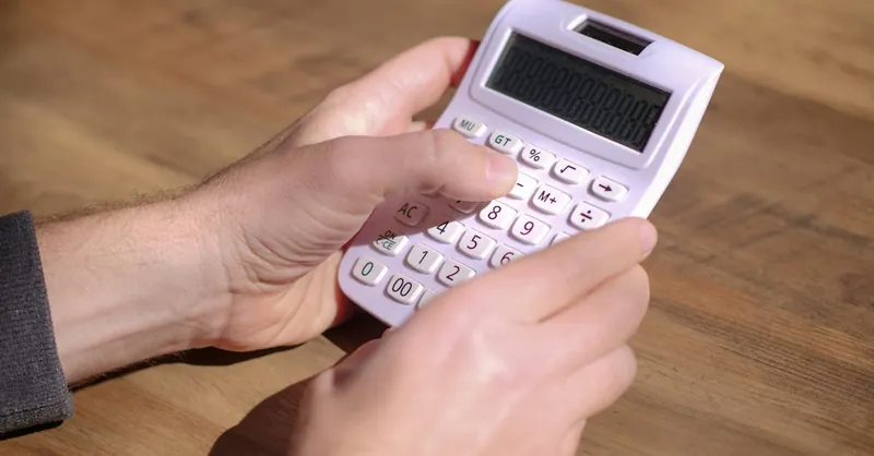 Hands using a pink calculator on a wooden table, emphasizing calculation and mathematics.