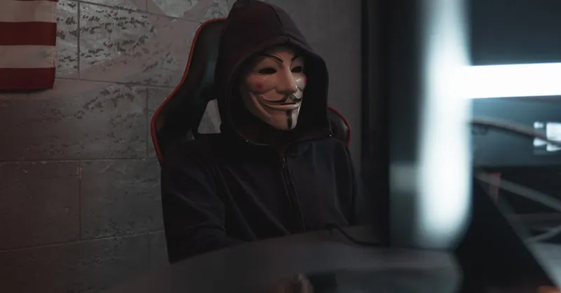 A mysterious person in a Guy Fawkes mask working at a computer, symbolizing cyber security themes.