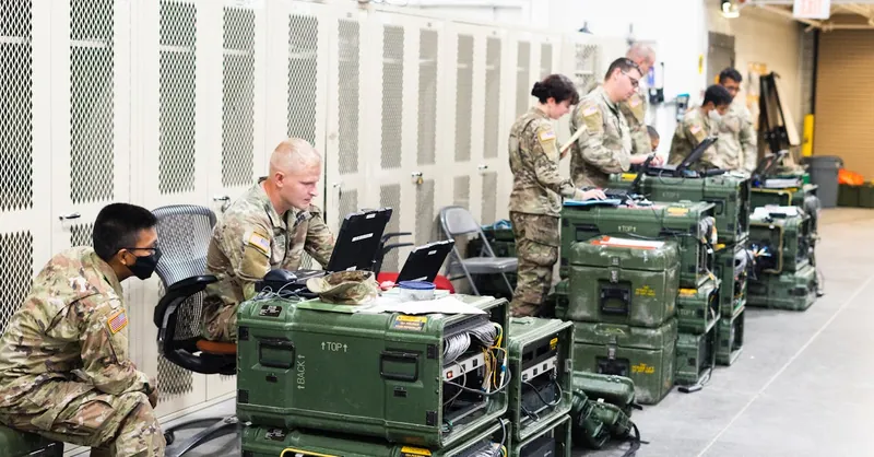 A group of military personnel in uniforms using computers and communication equipment in a secure indoor facility.
